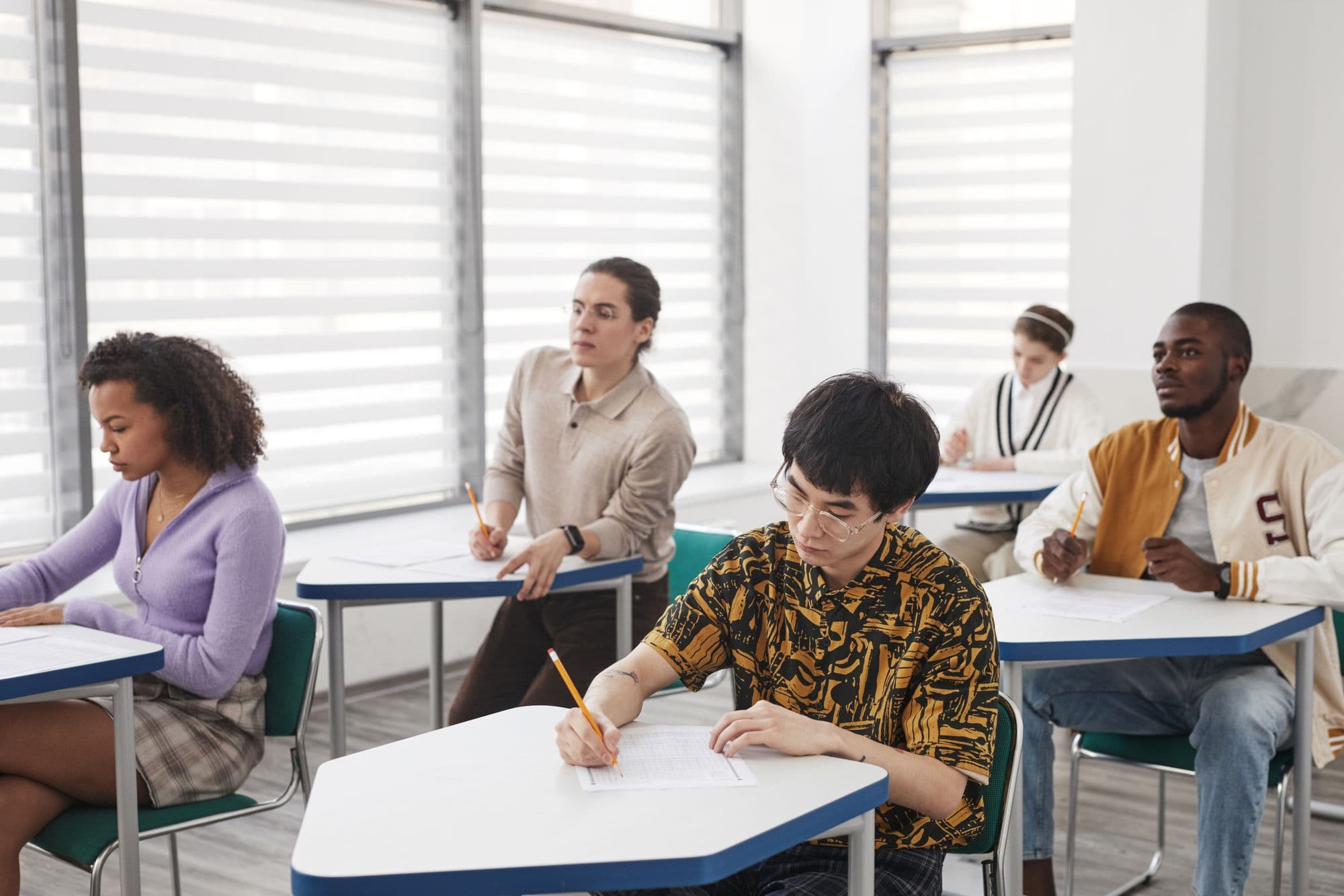 Students sitting an exam at spaced desks while an invigilator watches